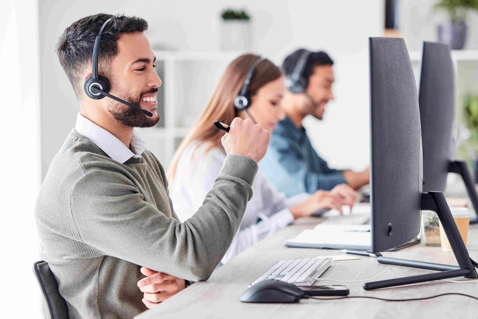 man in the office with a headset smiling at a desktop computer